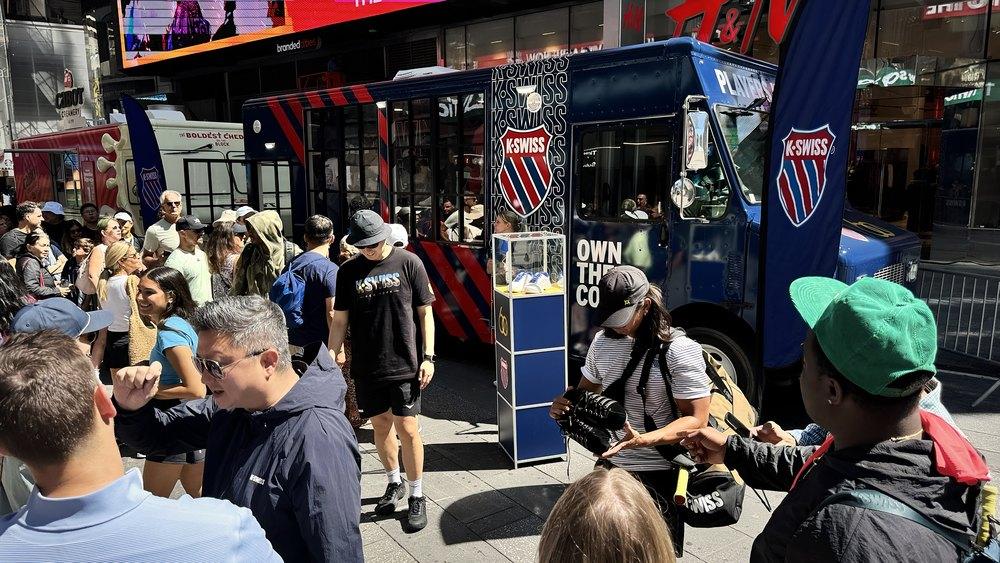 Crowds gather around a navy branded sneaker truck with a product display case in Times Square